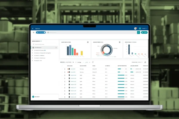 Mobile device management dashboard showing device analytics, battery levels, and OS data on a laptop screen in a warehouse setting.