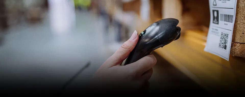 Hand scanning a barcode label on a warehouse shelf for inventory control using a handheld barcode scanner.