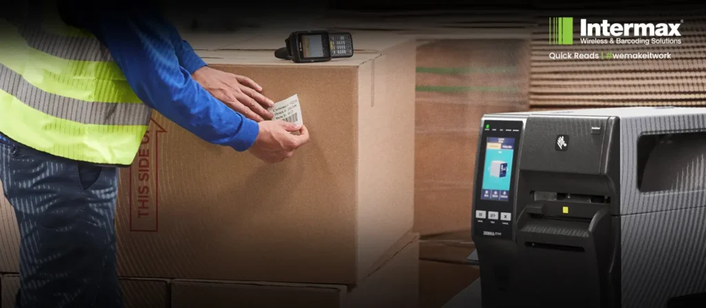 Worker applying barcode label to warehouse carton beside Zebra industrial thermal printer for high-volume warehouse labelling